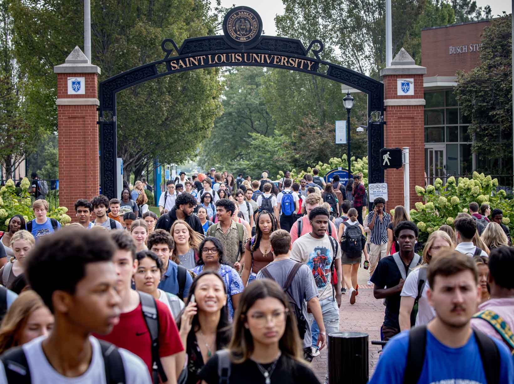A crowd of students walks on a path through a campus gateway