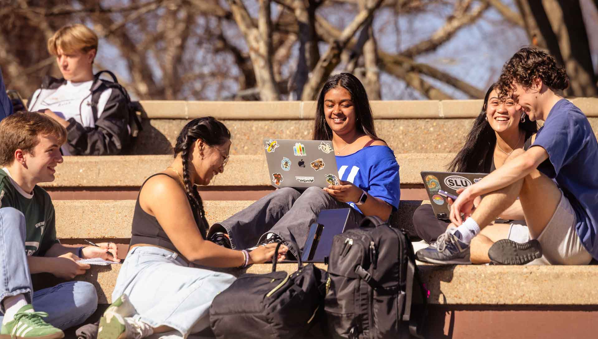 Students seated on outdoor stairs talk and smile