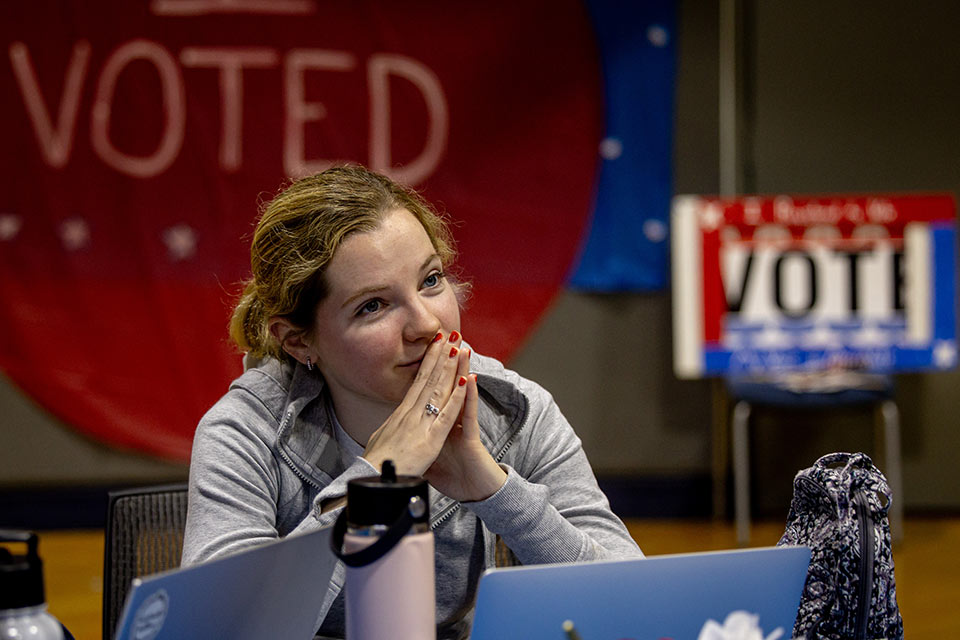 Blonde female student sits in front of two voting signs Student on election night